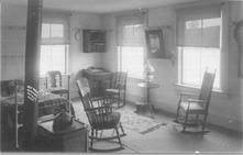 SA1324.3 - Photo shows an iron bed, three rocking chairs, a side chair, stove, desk, mirror, and small hanging bookrack. Identified on the front., Winterthur Shaker Photograph and Post Card Collection 1851 to 1921c